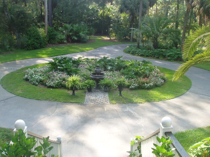 a circular garden in the middle of a driveway surrounded by lush green trees and bushes