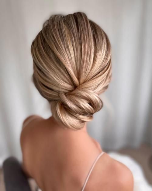 a woman with blonde hair in a low bun, sitting on a bed and looking off to the side