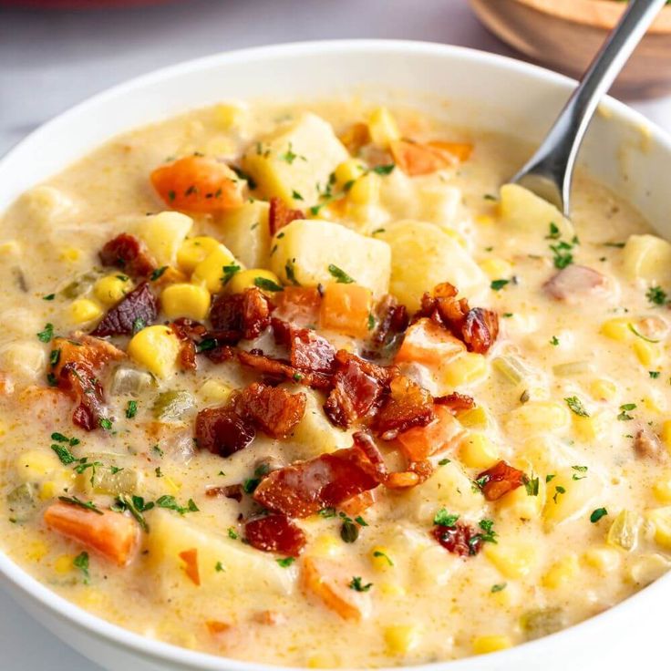 a white bowl filled with corn, potatoes and bacon chowder on top of a table