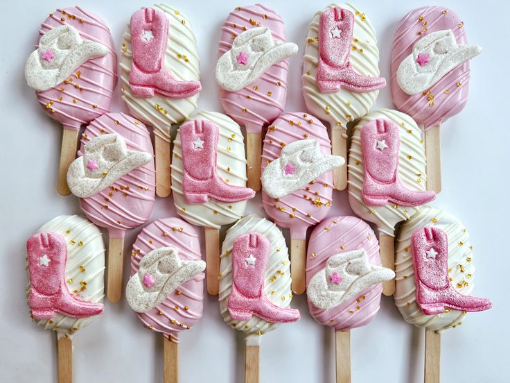 pink and white decorated cookies are arranged on wooden skewers with baby booties