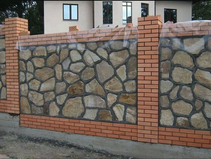 a brick wall with some rocks on the top and bottom part, behind it is a house