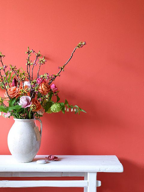 a white vase filled with lots of flowers on top of a table next to a pink wall