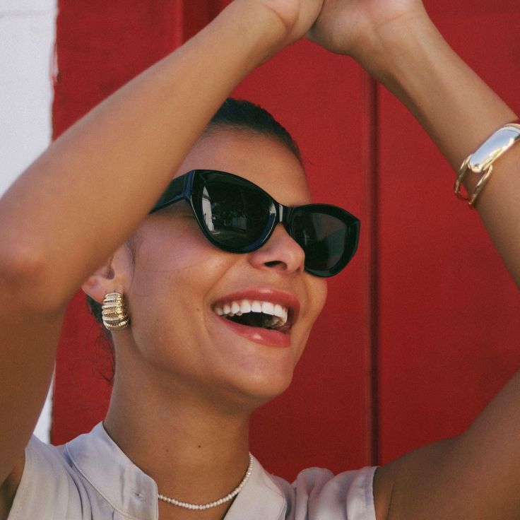 a woman wearing sunglasses is smiling and holding her hair up