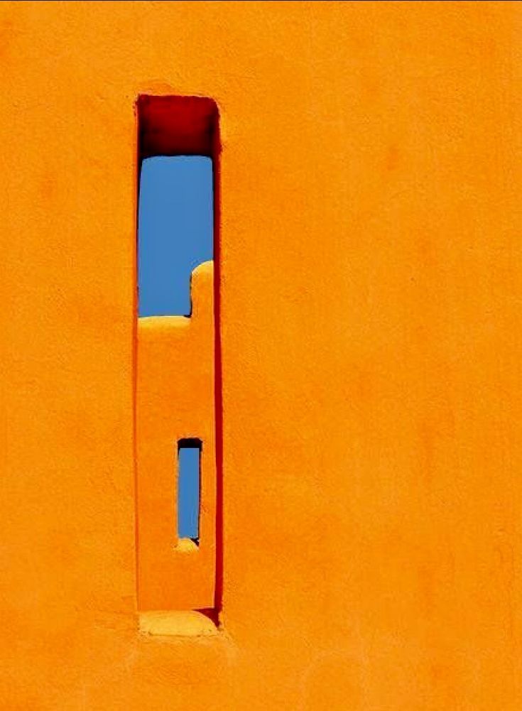 an orange wall with a small window in the center and blue sky behind it on a sunny day