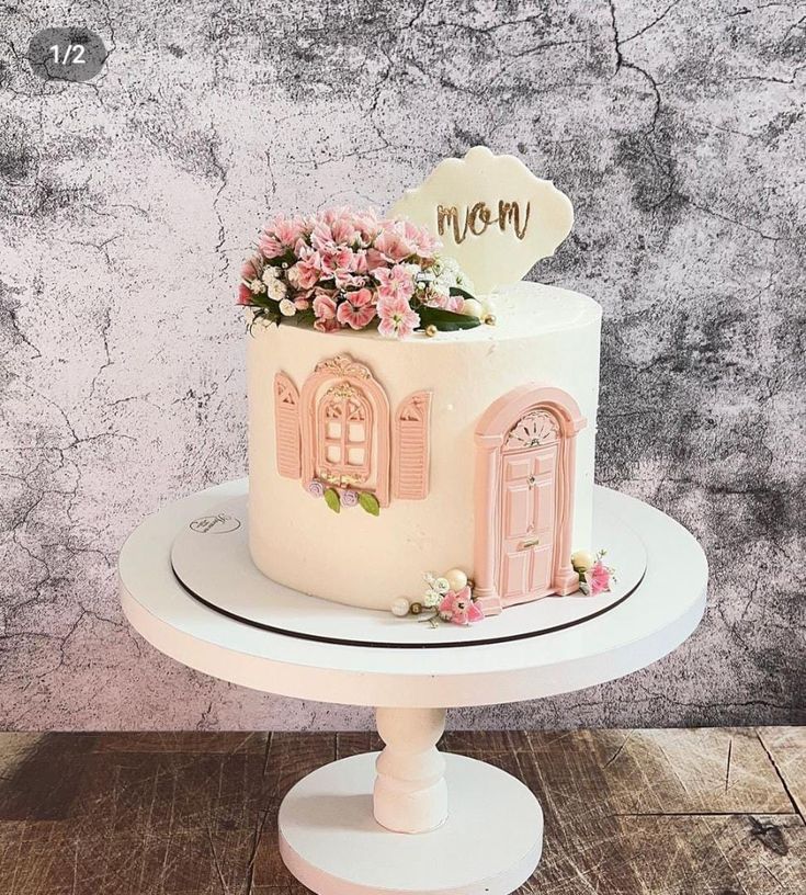 a white cake with pink flowers and a sign that says mom on the top is sitting on a pedestal