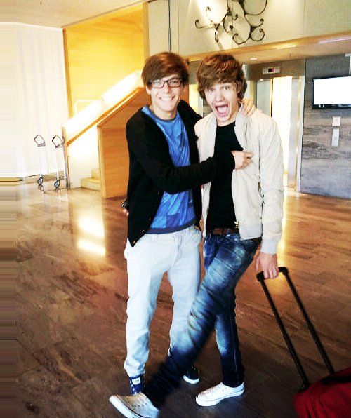 two young men standing next to each other in an empty room with luggage on the floor