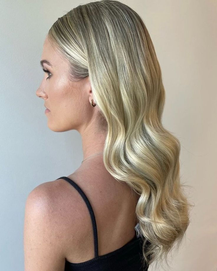 a woman with long blonde hair standing in front of a wall and looking off to the side