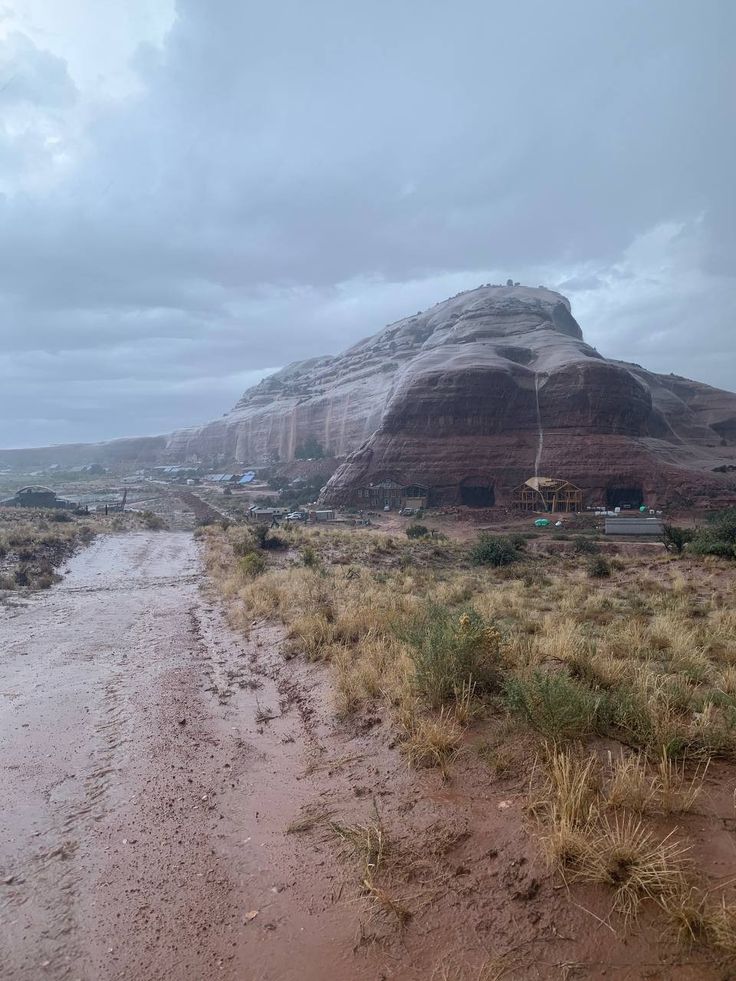 a dirt road in front of a large rock outcropping on a cloudy day