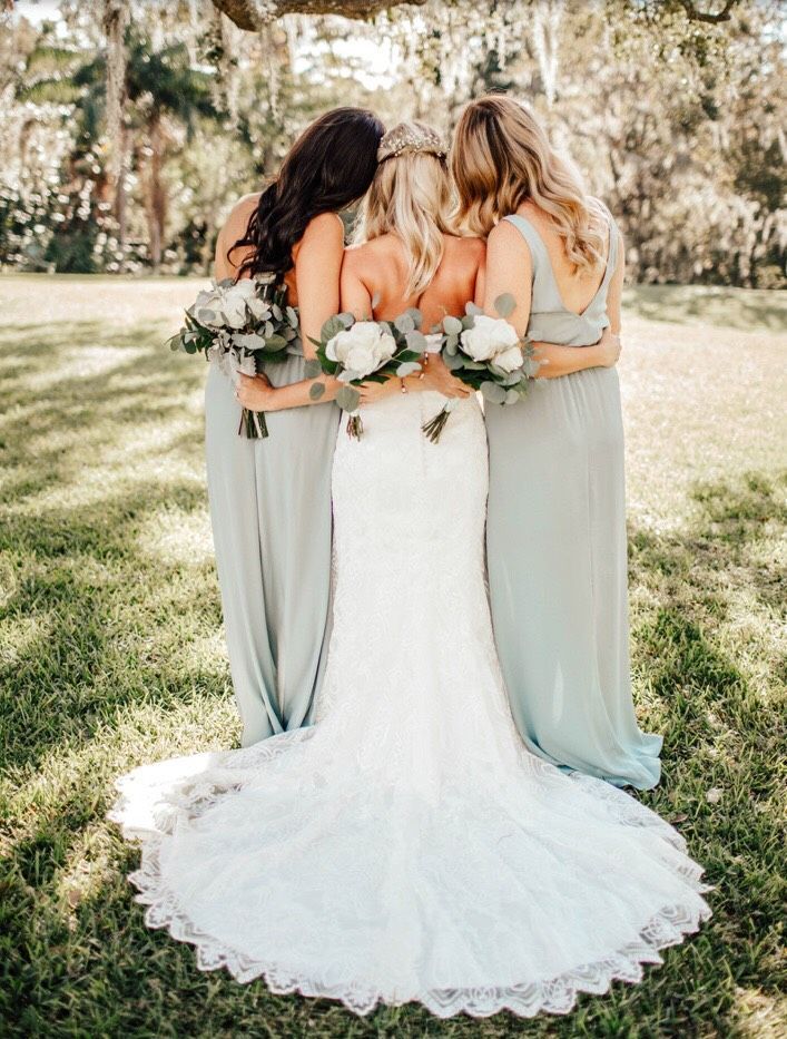 three bridesmaids hugging each other in front of a large oak tree with greenery