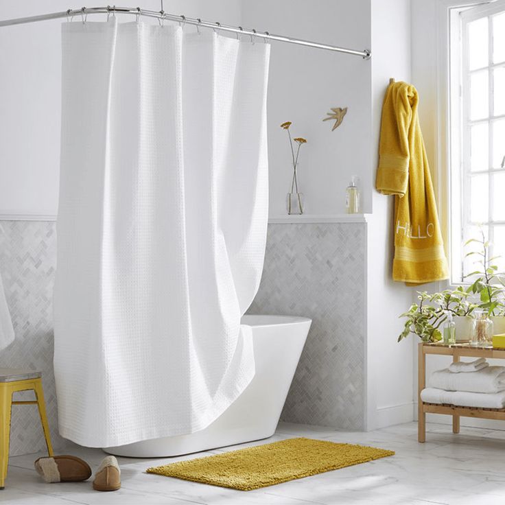 a white bathroom with yellow accents and towels on the shower curtain, rugs and bathtub