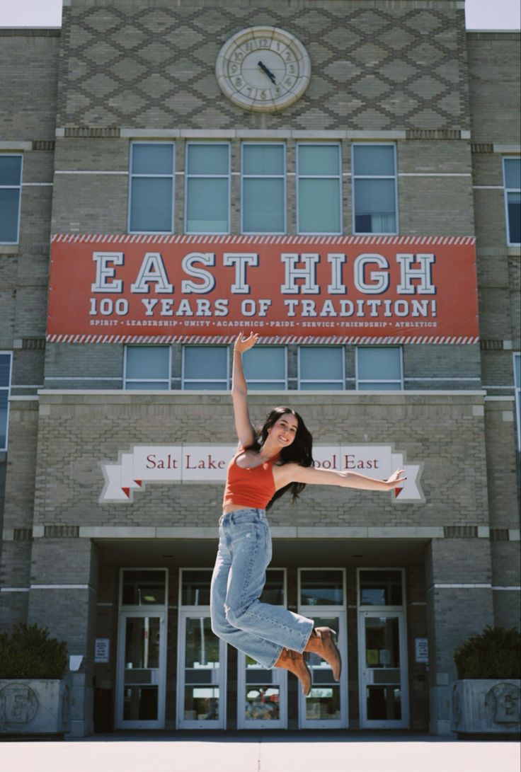 a woman jumping in the air with her arms up and legs spread wide outside an east high school