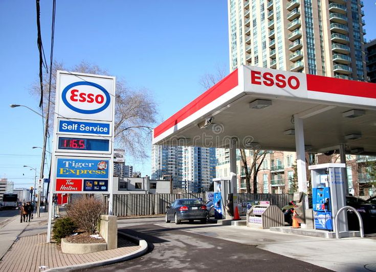 an esso gas station with cars parked at it's entrance and buildings in the background