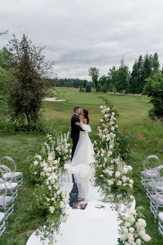 a bride and groom kissing in front of an outdoor ceremony setup with white flowers on the aisle