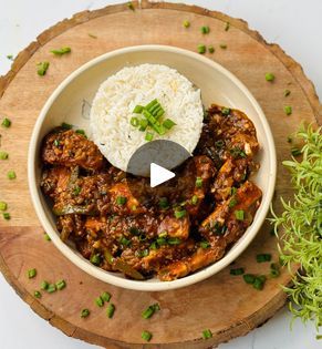 a bowl filled with rice and meat on top of a wooden cutting board next to a plant