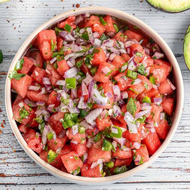 a bowl filled with watermelon and onions next to an avocado