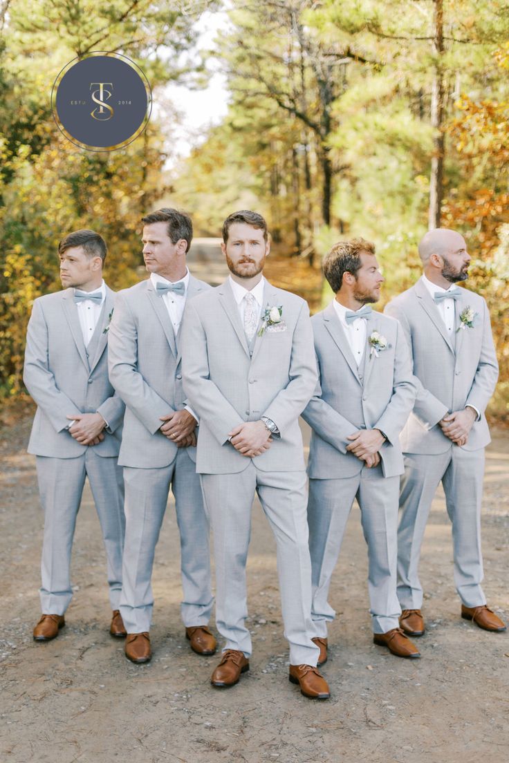 a group of men standing next to each other in front of trees and bushes with their hands on their hipss