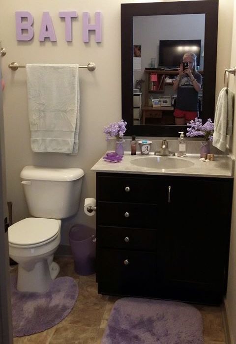 a bathroom with a toilet, sink and mirror in it's corner next to a purple rug on the floor