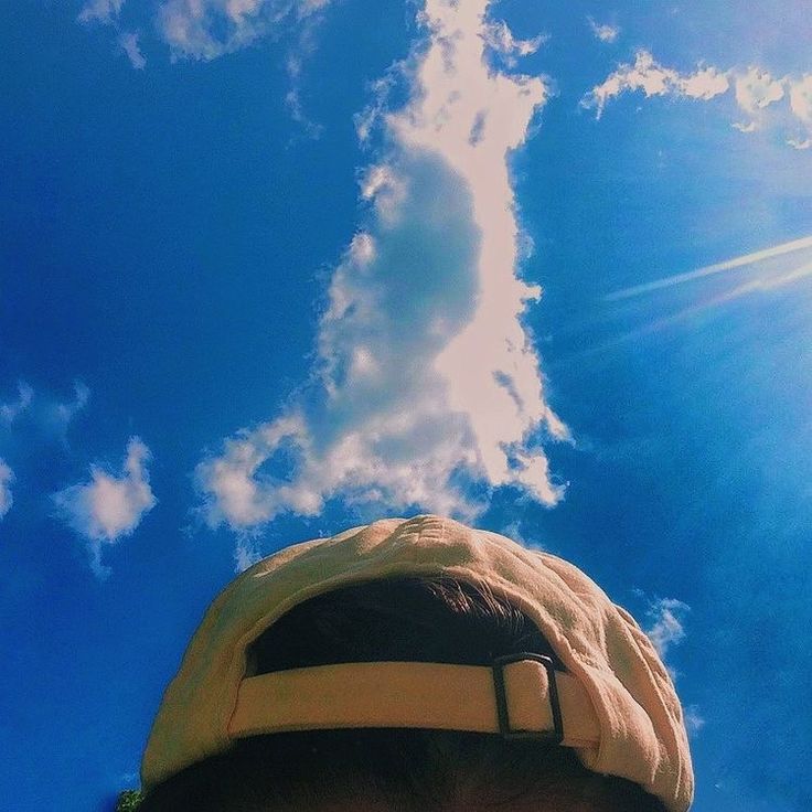 a man wearing a hat looking up into the sky with clouds in the back ground