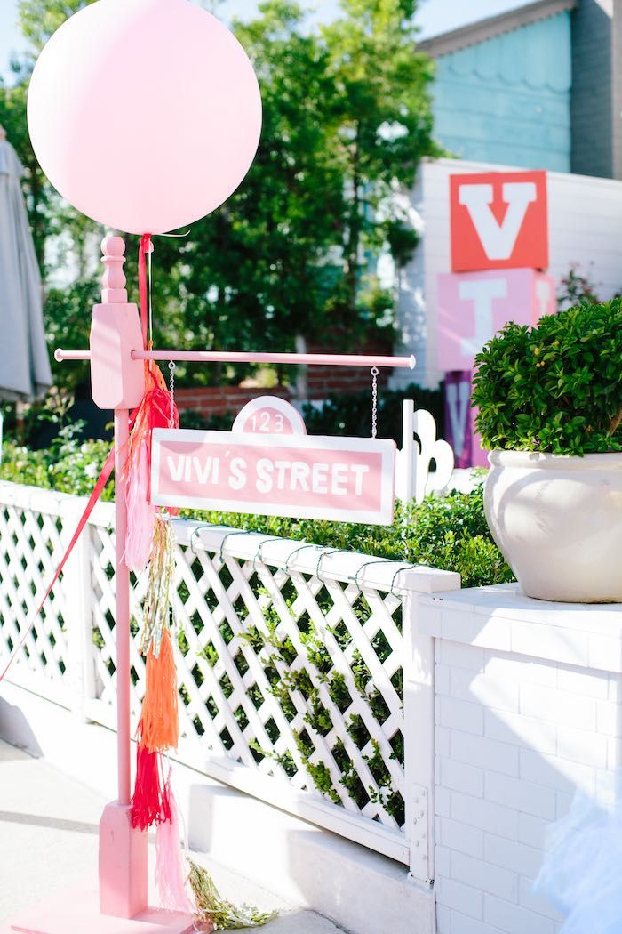 a pink street sign with tassels hanging from it's sides and a white fence in the background