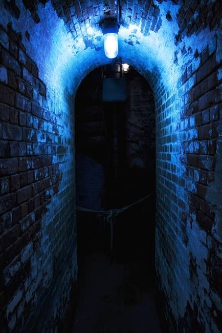 a dark tunnel with blue light at the end and brick walls on both sides that are lit up