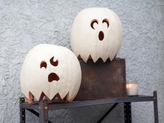 two carved pumpkins with faces on them sitting on a shelf next to a candle