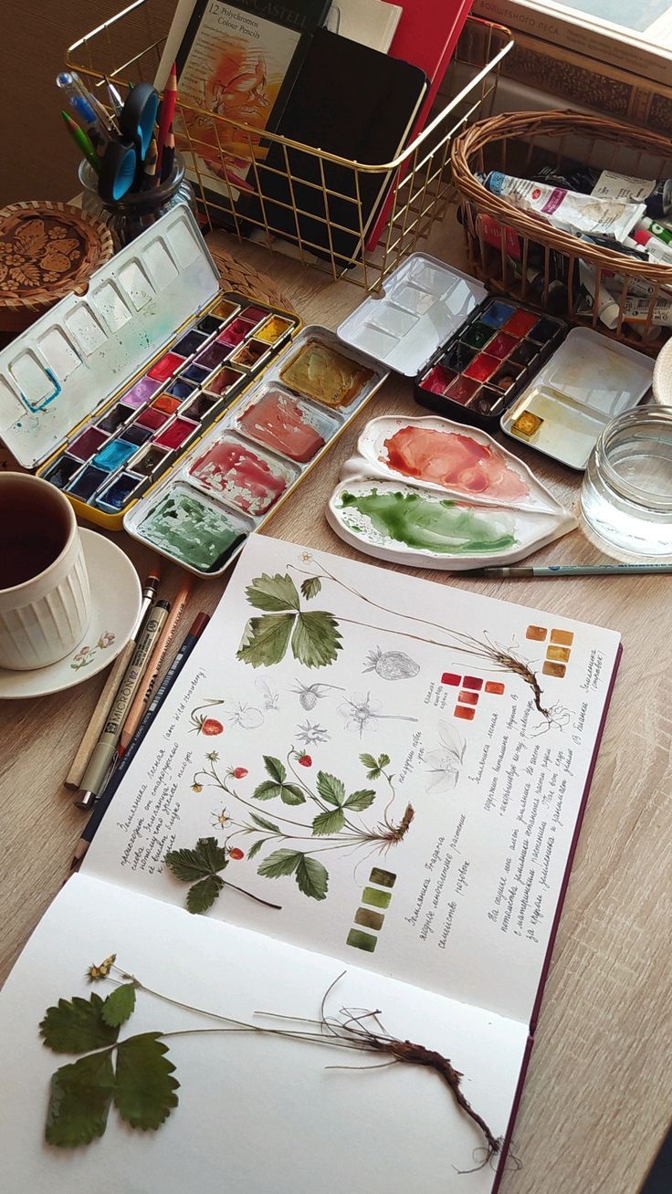 an open book sitting on top of a wooden table next to paint brushes and paints