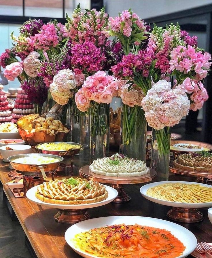 a table topped with lots of different types of foods and flowers in vases next to each other