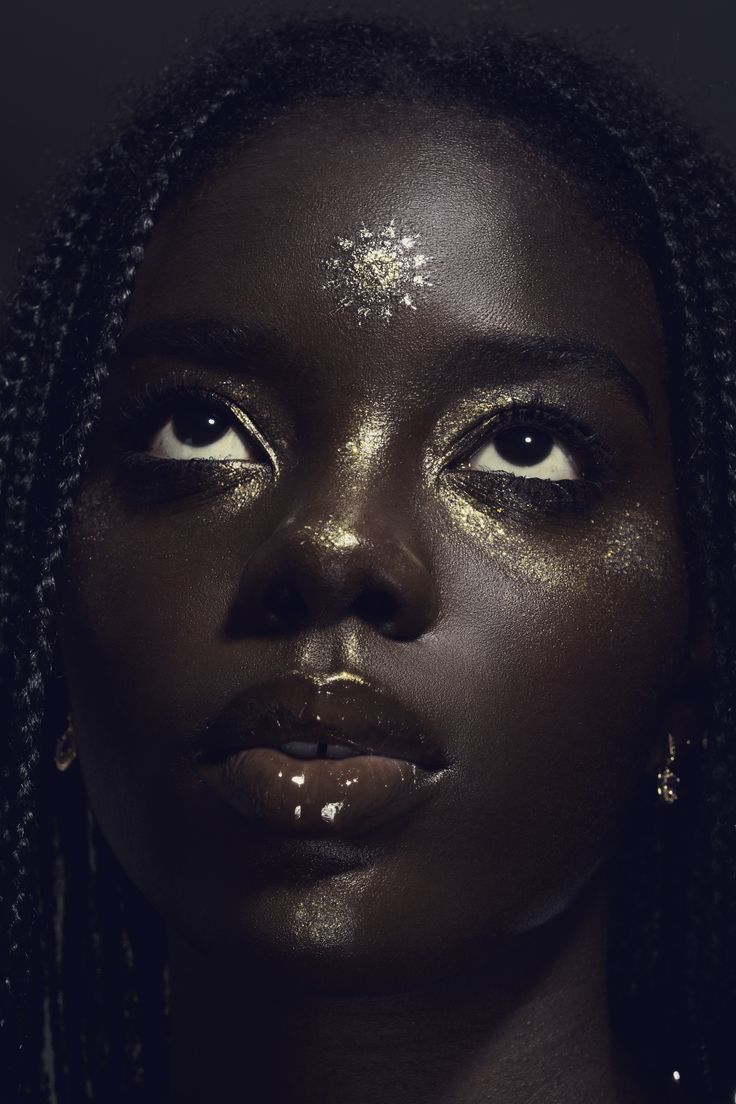 a woman with gold glitter on her face and long dreadlocks, looking at the camera