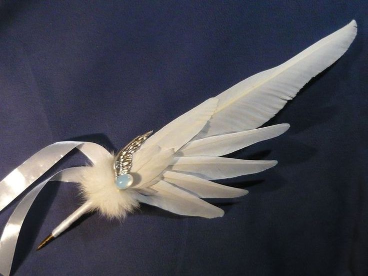 a white feather and crystal brooch on a blue cloth with silver ribbon around it