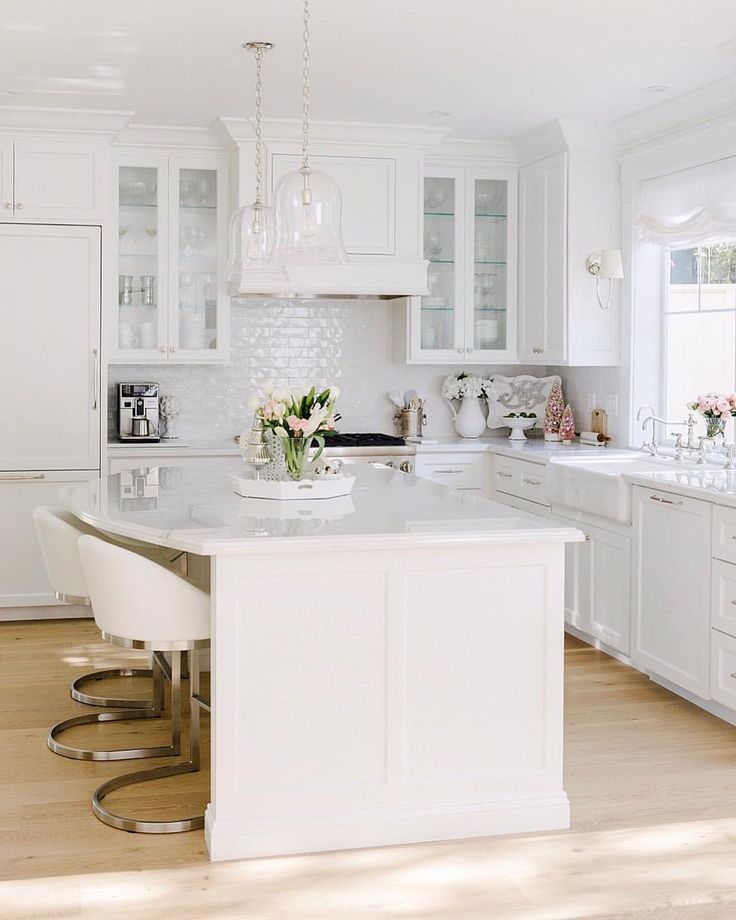 a large kitchen with white cabinets and counter tops, along with two bar stools