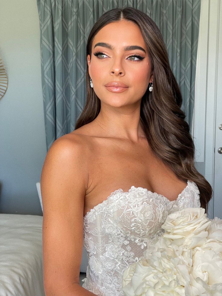 a woman in a wedding dress holding a bouquet of flowers and posing for the camera