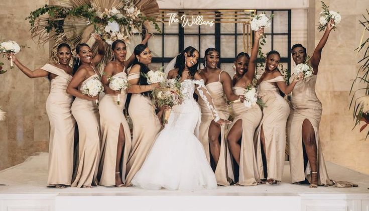 a group of women standing next to each other in front of a wall holding bouquets