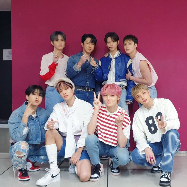 the group of young men are posing together in front of a pink wall with their hands up