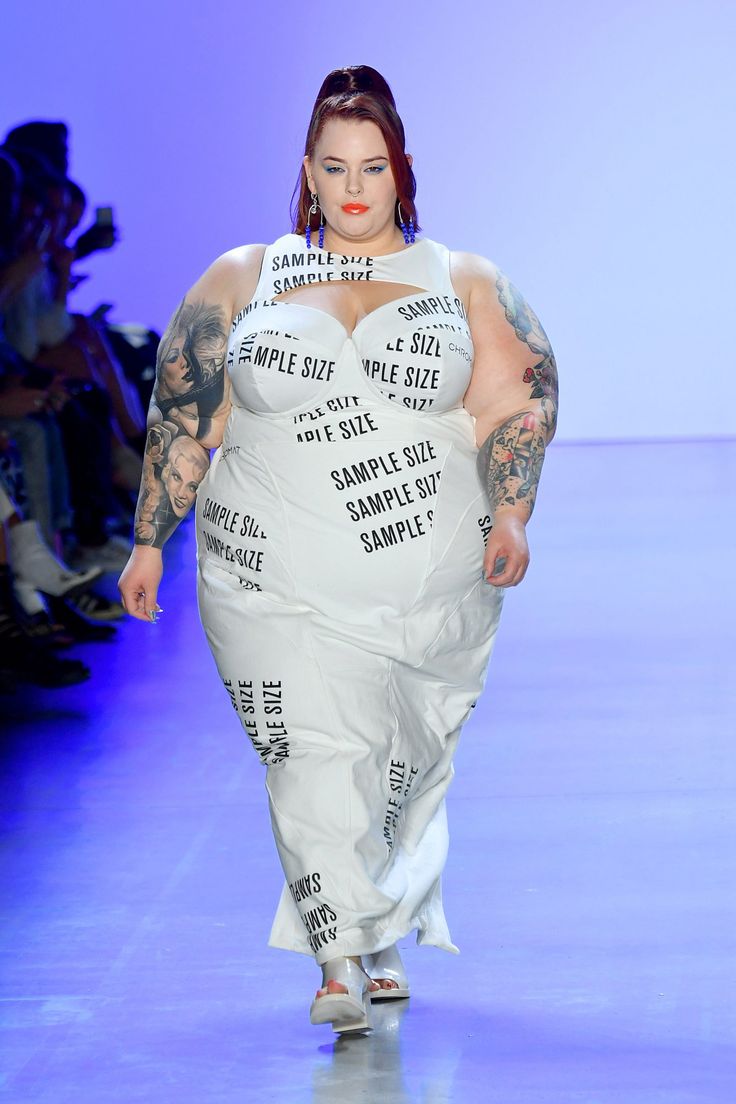 a woman walking down a runway wearing a white dress with lots of writing on it