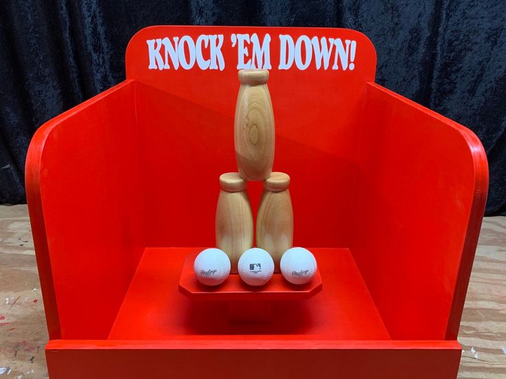 a red chair with three wooden bowling balls in it and a sign that says knock em down