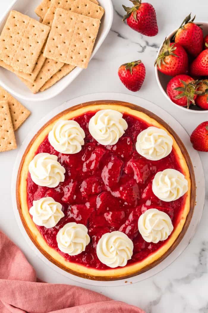 a strawberry cheesecake with whipped cream on top and strawberries in bowls around it