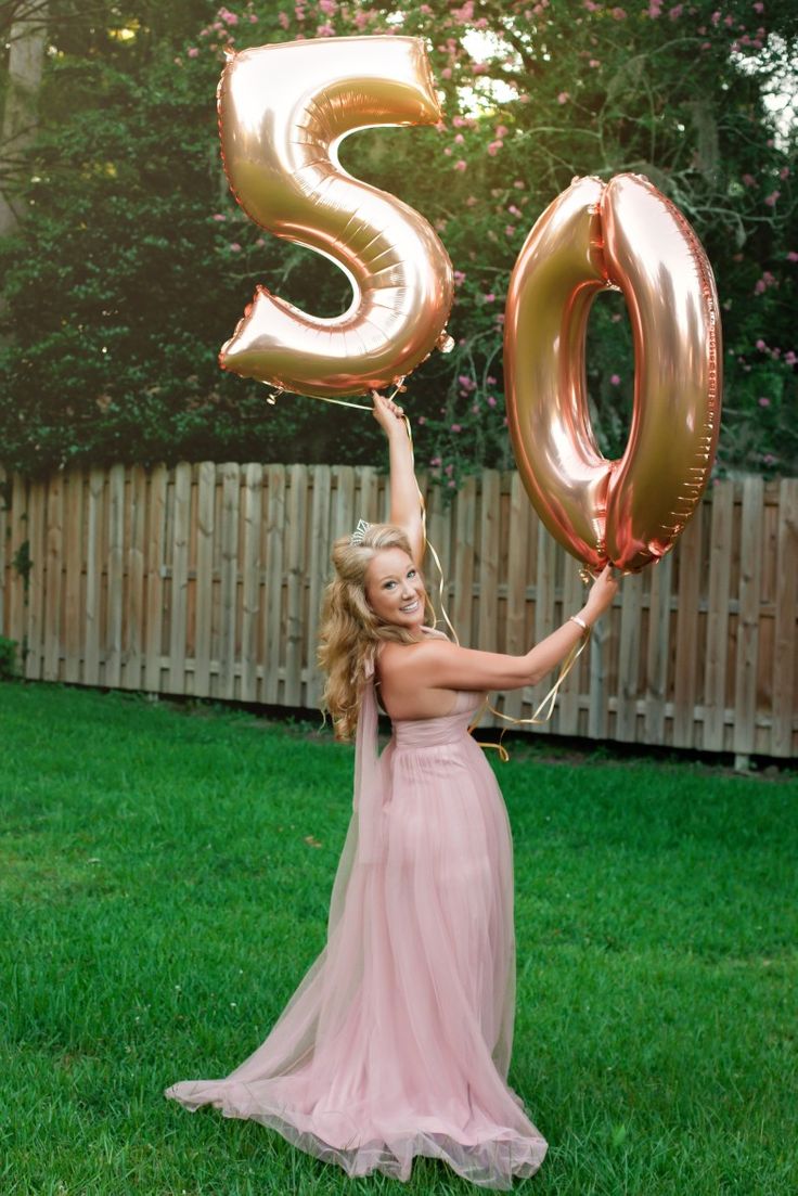 a woman in a pink dress holding two large gold balloons that spell the number 50