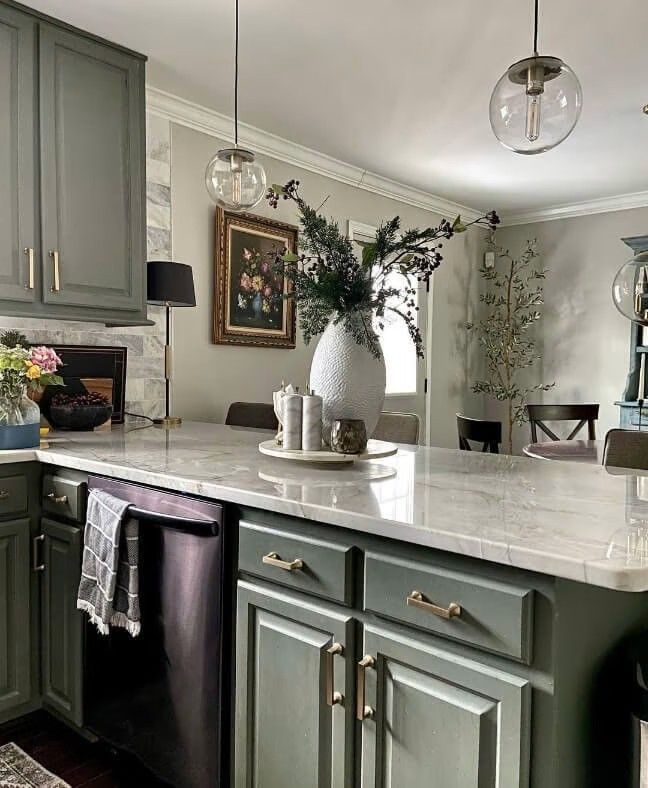 a kitchen with green cabinets and white marble counter tops, an island in the middle