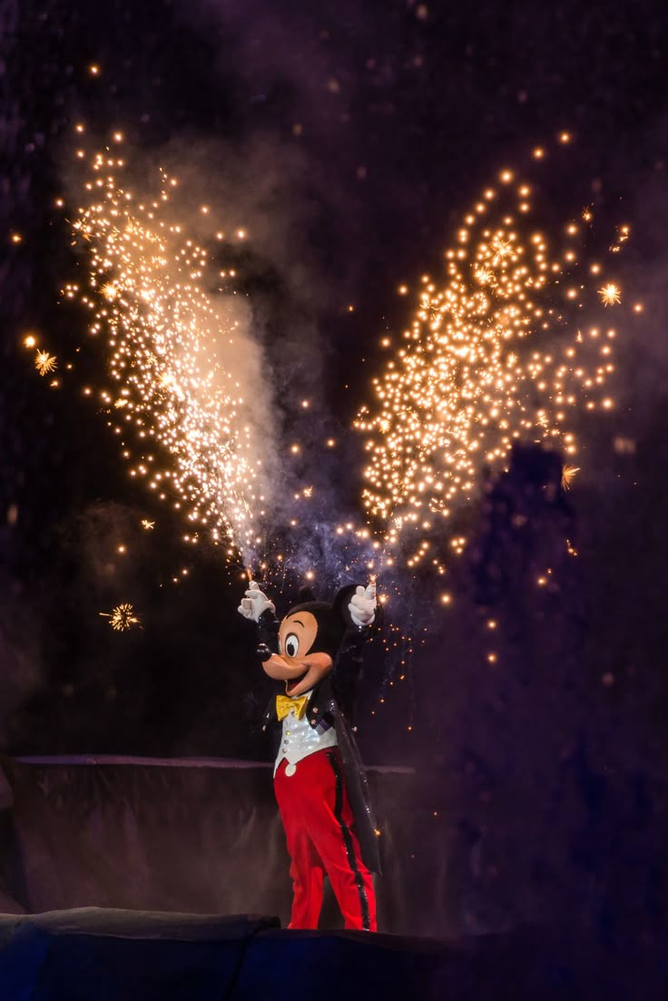 mickey mouse waving at fireworks in the night sky