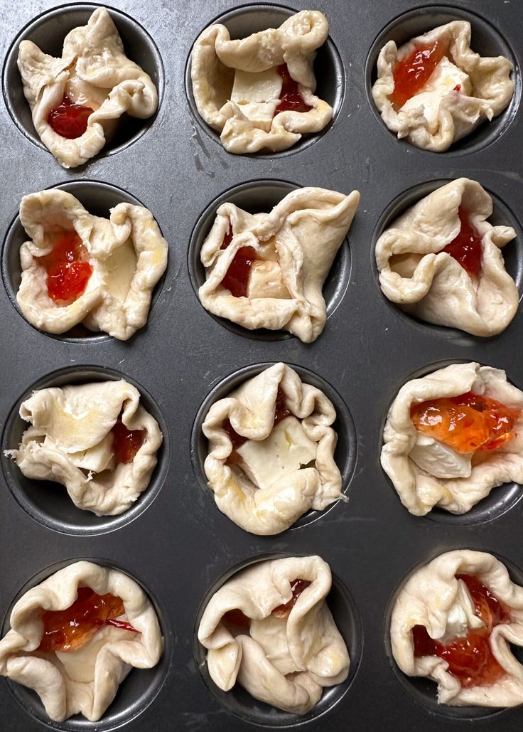 twelve uncooked dumplings in a muffin tin with jelly toppings on them