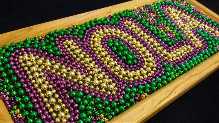 a wooden tray with beads on it and the word boo spelled out in gold, purple, and green