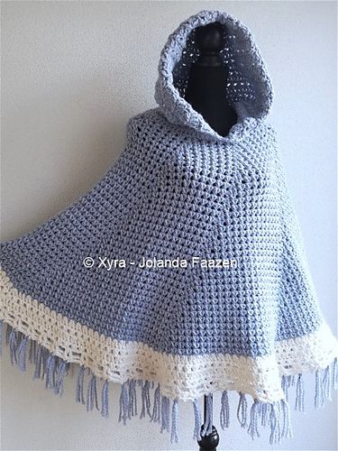 a blue and white crocheted ponchy with fringes hanging on a wall