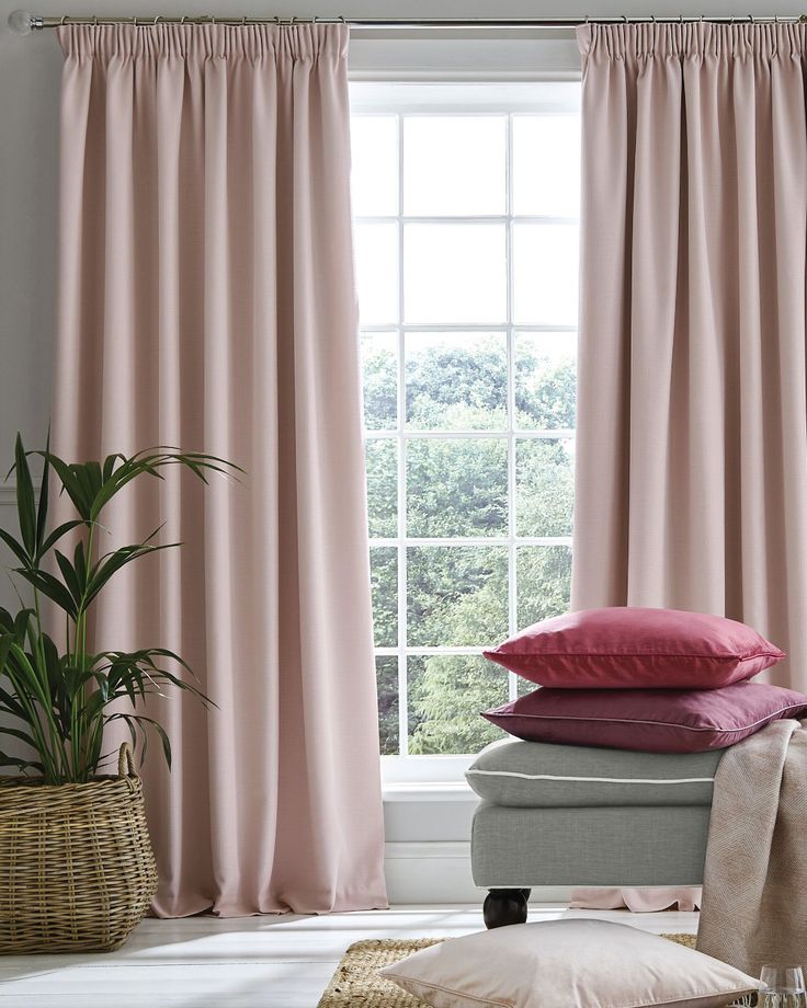 a window with pink curtains and pillows in front of it, next to a wicker basket