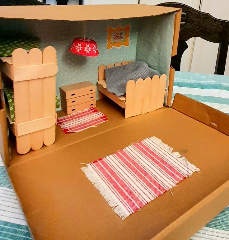 an open cardboard box on top of a bed with a doll house in the middle