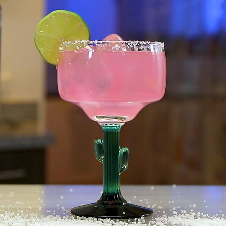 a pink drink with a lime slice on the rim in a green glass sitting on a counter