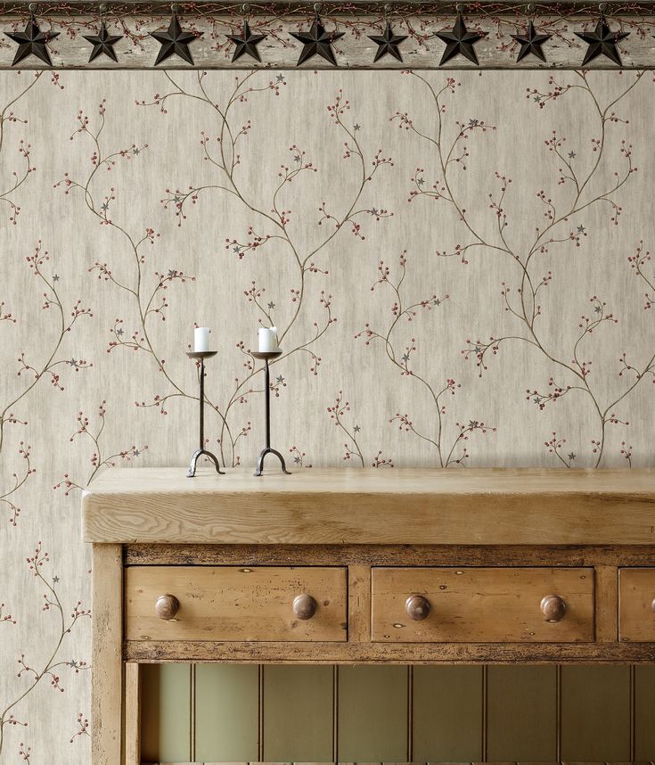 two candles sit on top of a wooden table in front of a floral wallpaper