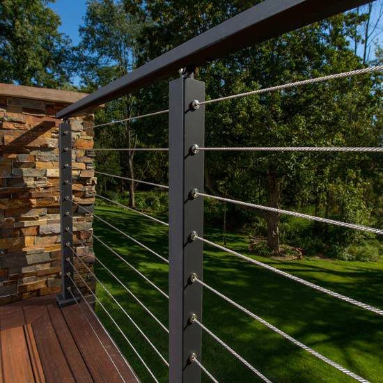 a wooden deck with metal railings next to a stone wall and green grass area