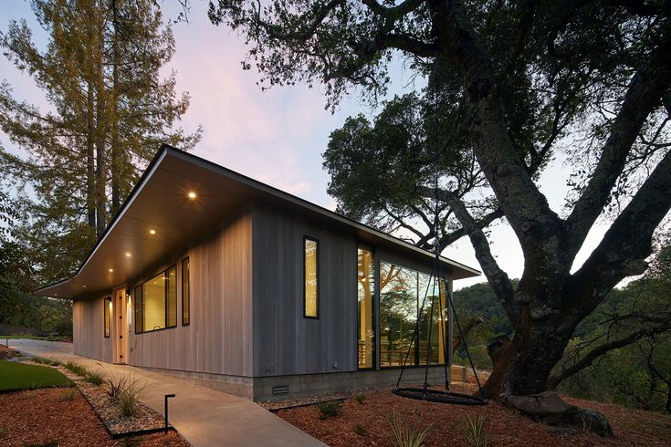 a modern house in the woods with trees and walkway leading up to it's entrance