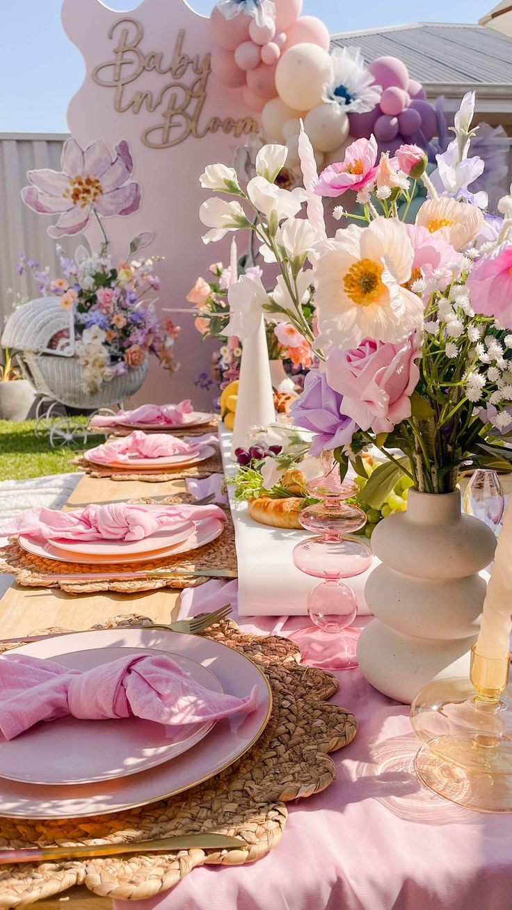 the table is set with pink and white flowers in vases, plates and napkins