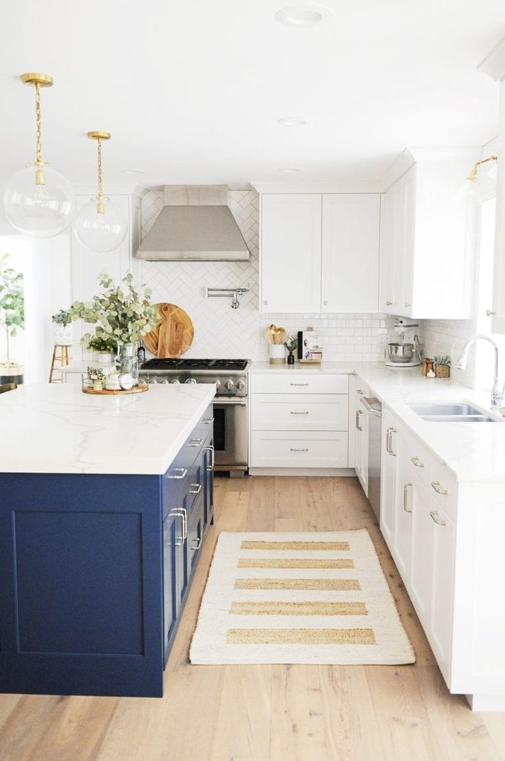 a kitchen with white cabinets and blue island in the center, along with an area rug on the floor